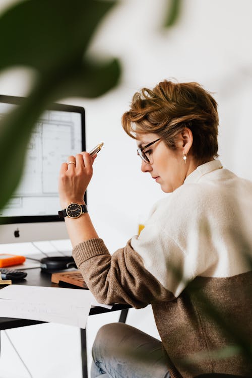 Side view of serious short haired adult female specialist in eyeglasses reading documents with concentration while working on project in modern office space