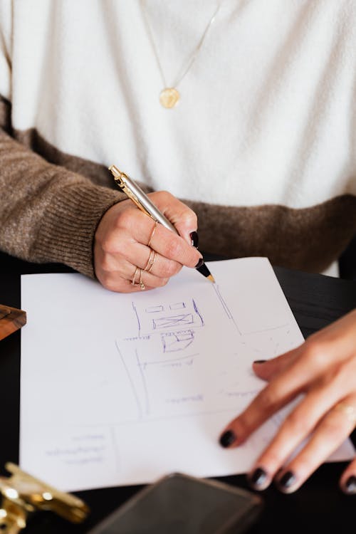 Crop unrecognizable female interior designer drawing sketchy plan of room of house sitting at desk