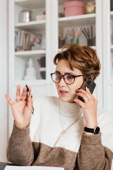 女商人拿着笔，在室内打电话时表情活跃地表达了担忧