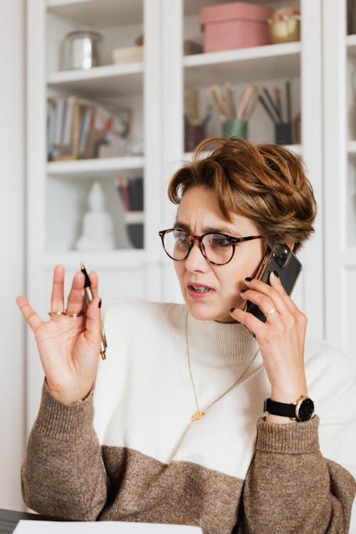 Free Businesswoman expressing concern while on a phone call indoors, holding a pen with an engaged expression. Stock Photo Free Businesswoman expressing concern while on a phone call indoors, holding a pen with an engaged expression. Stock Photo