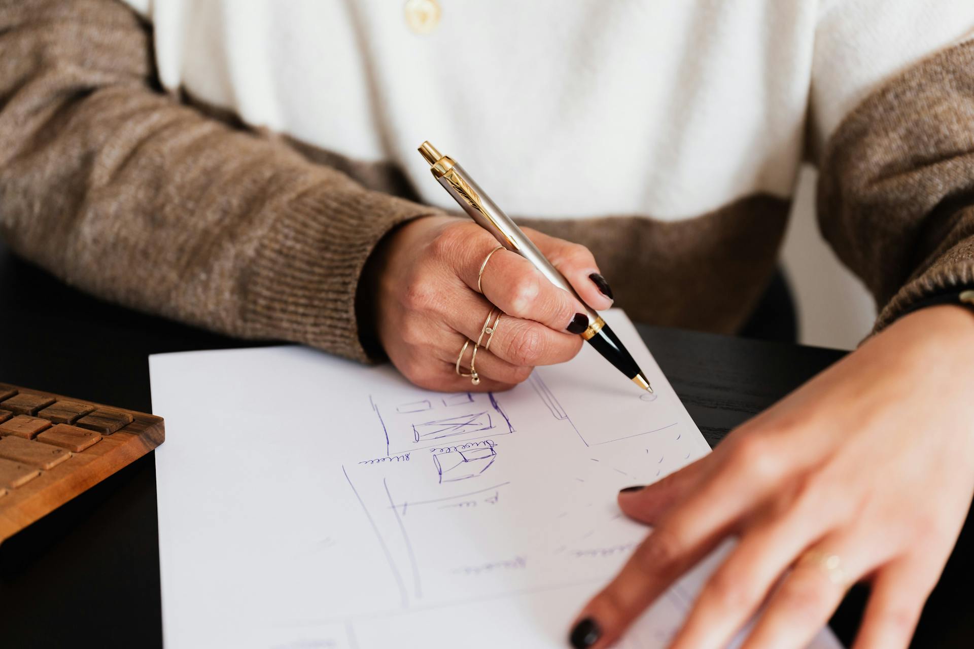 Crop anonymous elegant lady drawing draft plan of room with pen sitting at computer desk