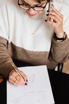 女设计师在办公桌前一边打电话，一边画草图，专注于工作