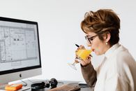 女建筑师坐在办公桌前，一边喝着果汁，一边专注地设计计算机方案