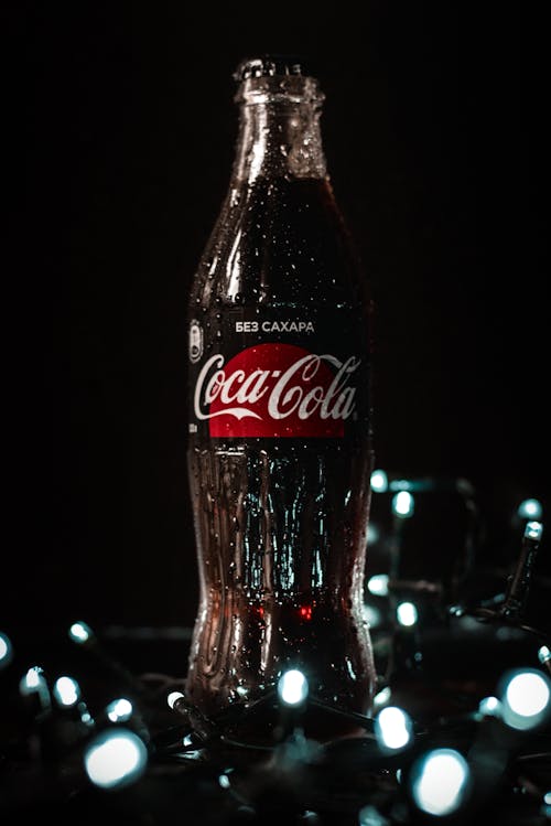 Bottle of refreshing soft drink on table near glowing lamps