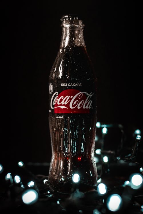 Free Glass bottle of cold cola with water drops placed on table near glowing garland against black background Stock Photo