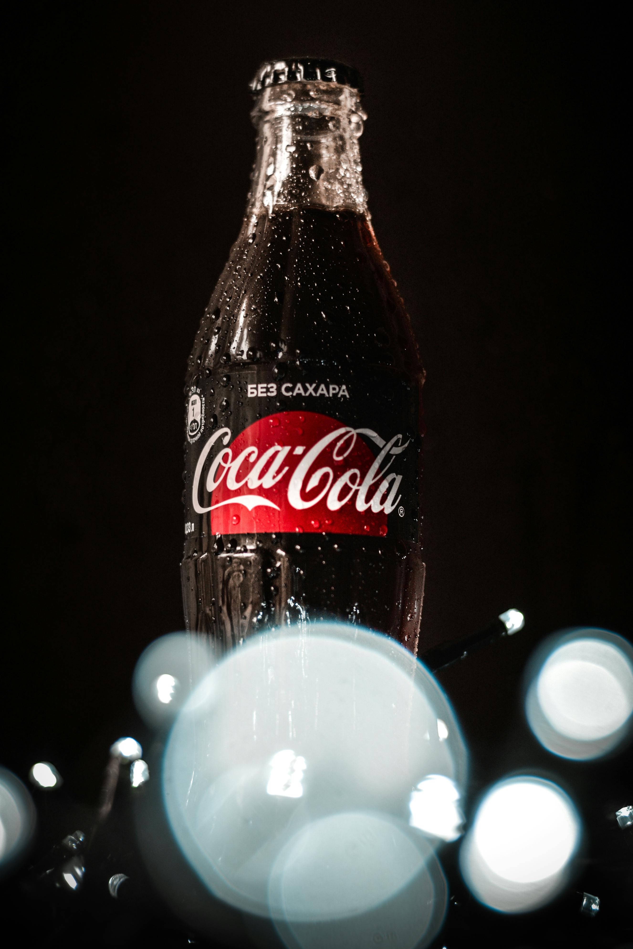 glass bottle of cold coke with glowing garlands on table