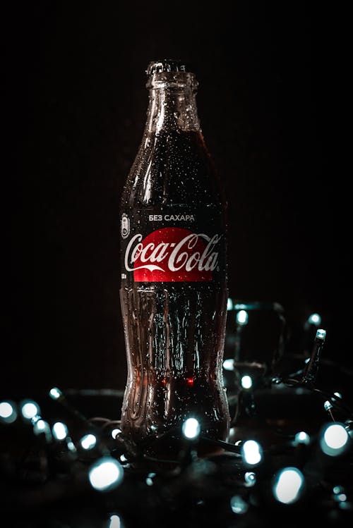 Cold glass bottle of refreshing soda arranged with glowing Christmas garlands on black table