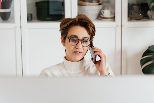 Smart woman in eyeglasses having phone conversation in modern office