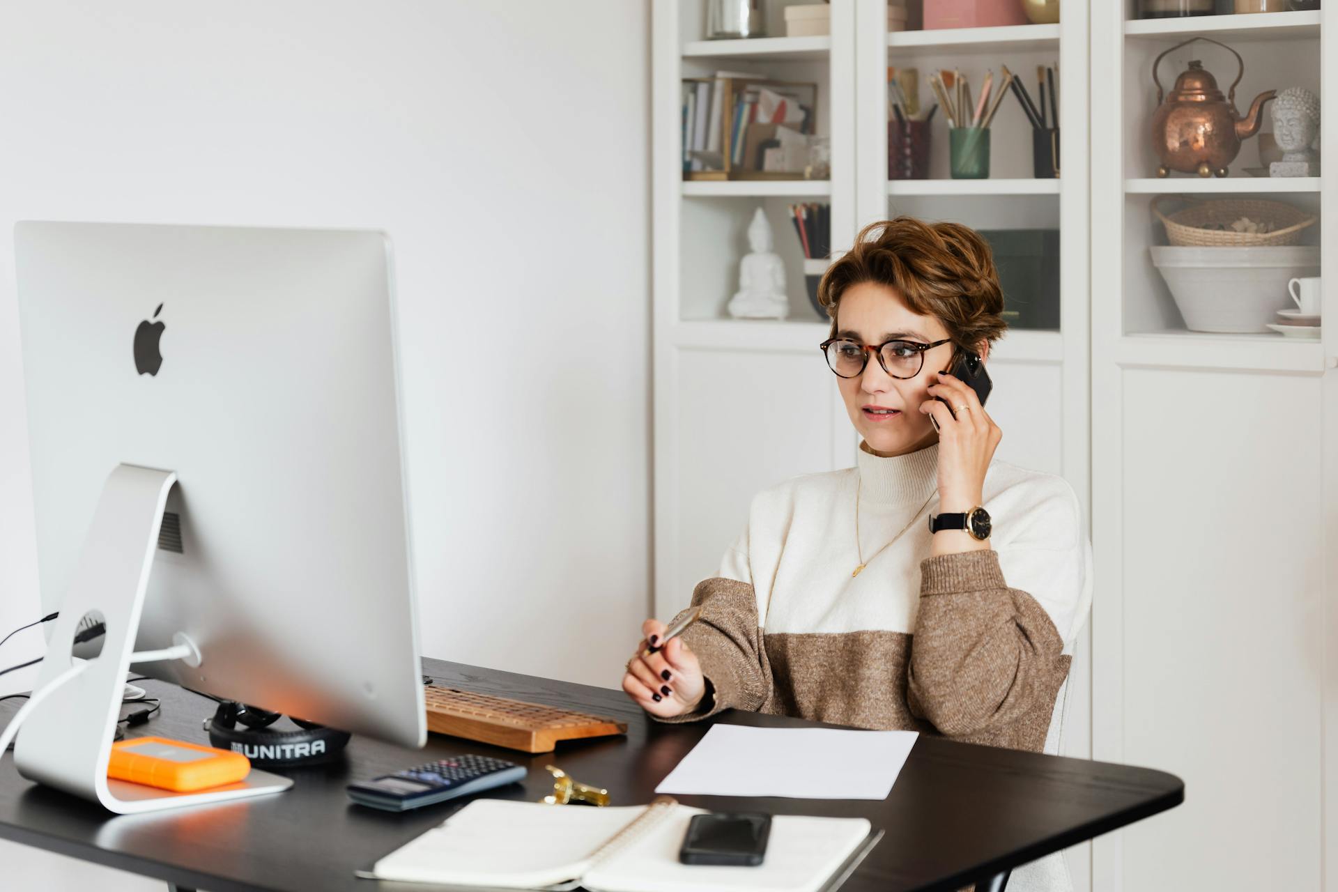 Smart confident female managing director listening to employees report on smartphone while working on computer in light modern office