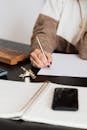 Unrecognizable female entrepreneur writing on piece of paper while sitting at table with notebook and smartphone