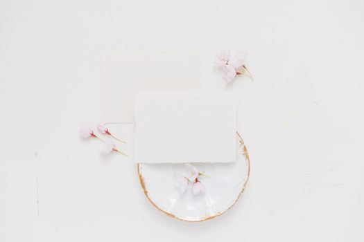 Delicate cherry blossoms on blank cards and ceramic plate in a soft minimalist flat lay.