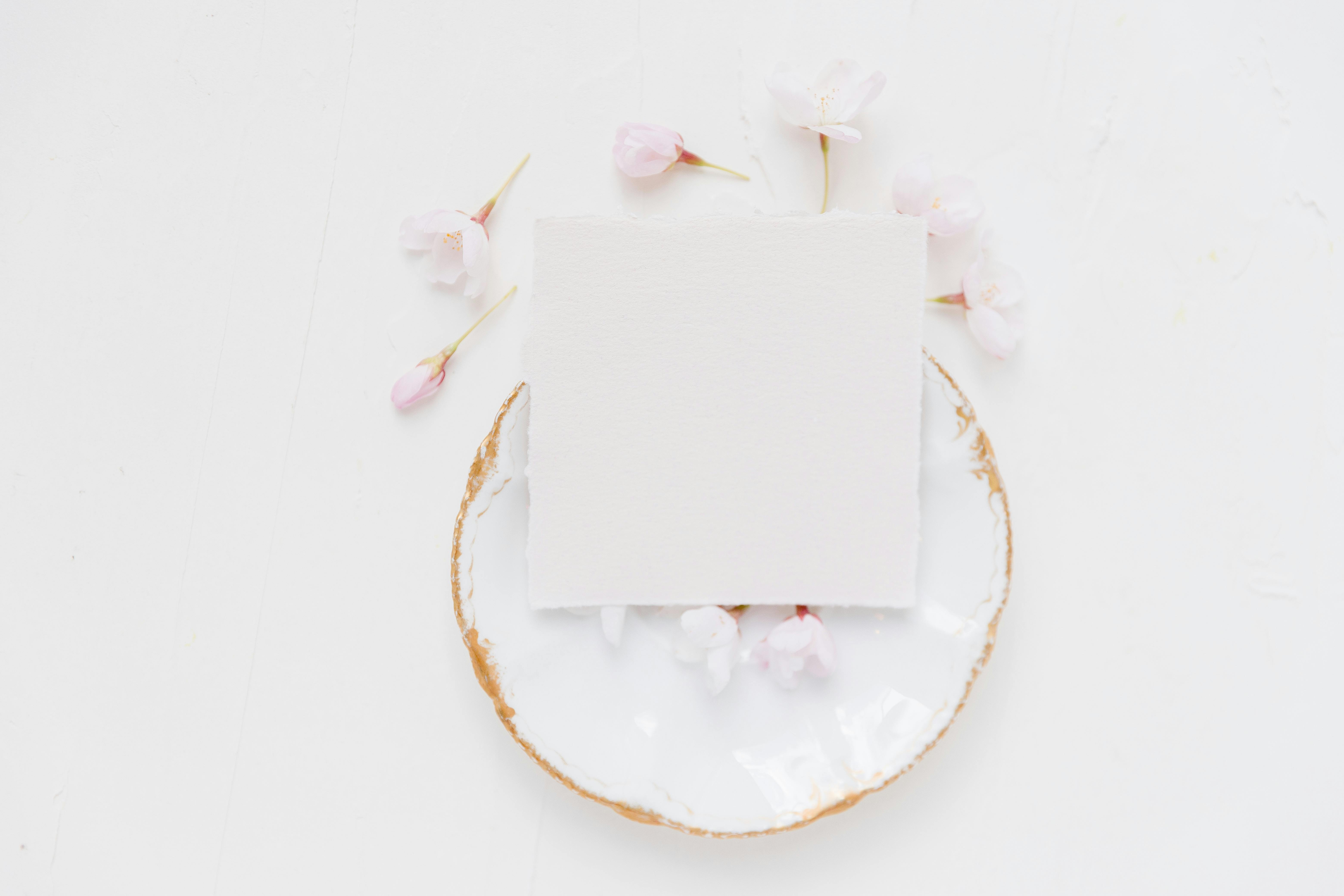 Elegant minimalist mockup featuring a blank card on a ceramic plate surrounded by delicate flowers.