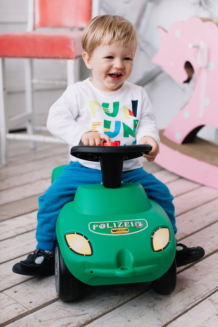 Boy In White Long Sleeve Shirt Riding On Green And Black Toy Car