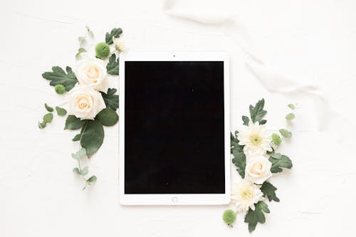 White Ipad on White Background Beside Blooming Flowers