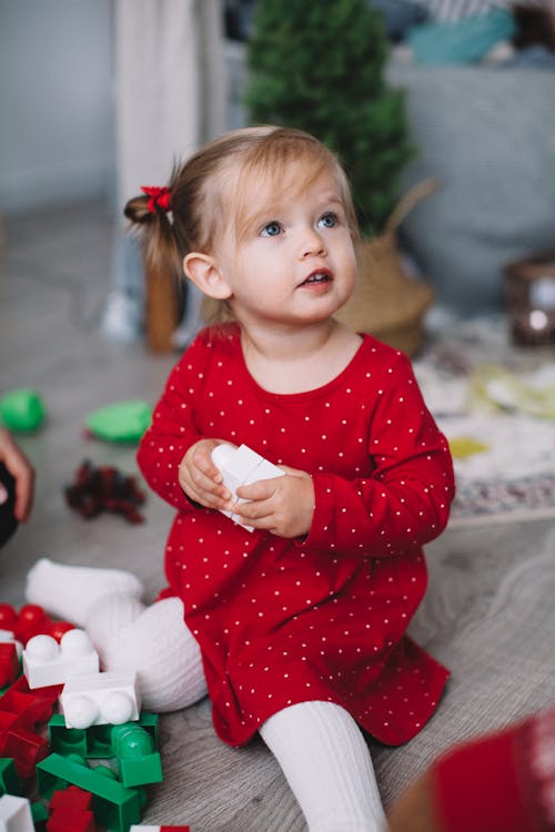 Baby Girl in Red and White Polka Dot Dress Sitting on Floor Playing with Plastic Toys