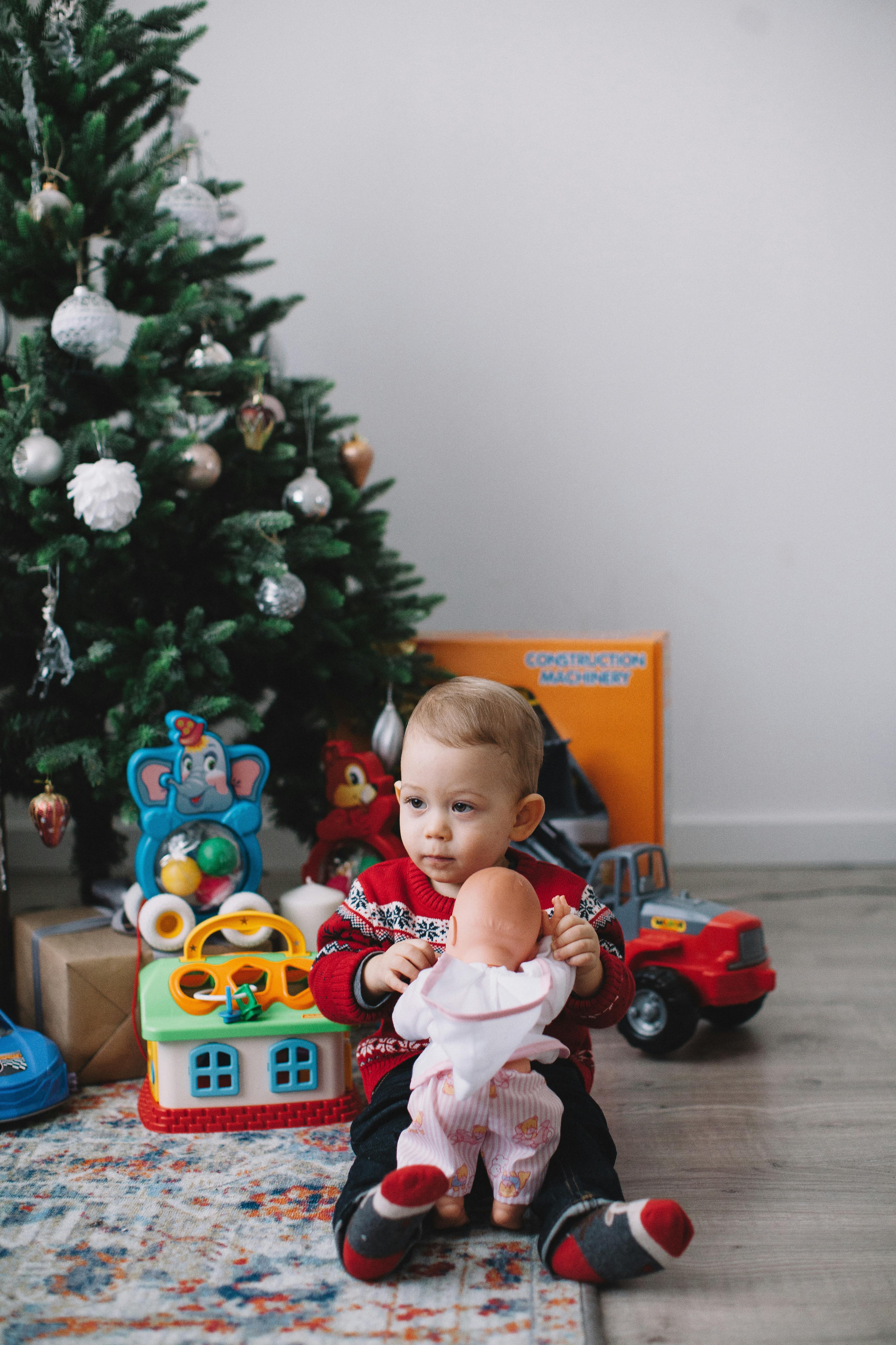 a young boy sitting on floor beside christmas tree