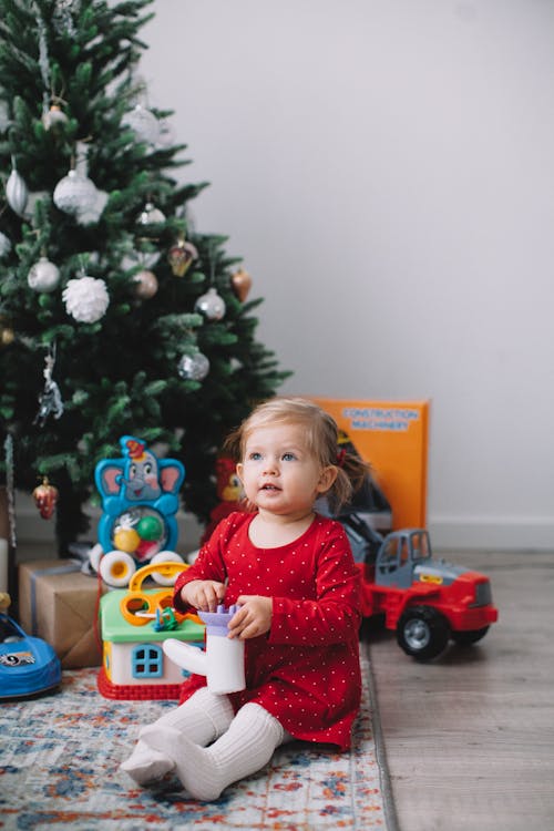 A Young Girl in Red Dress Sitting Beside the Christmas Tree