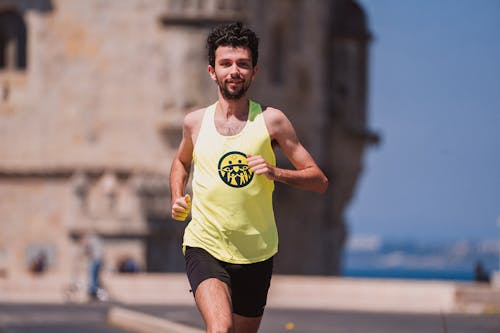 Positive young male sprinter in activewear running alone on street of coastal town during morning workout