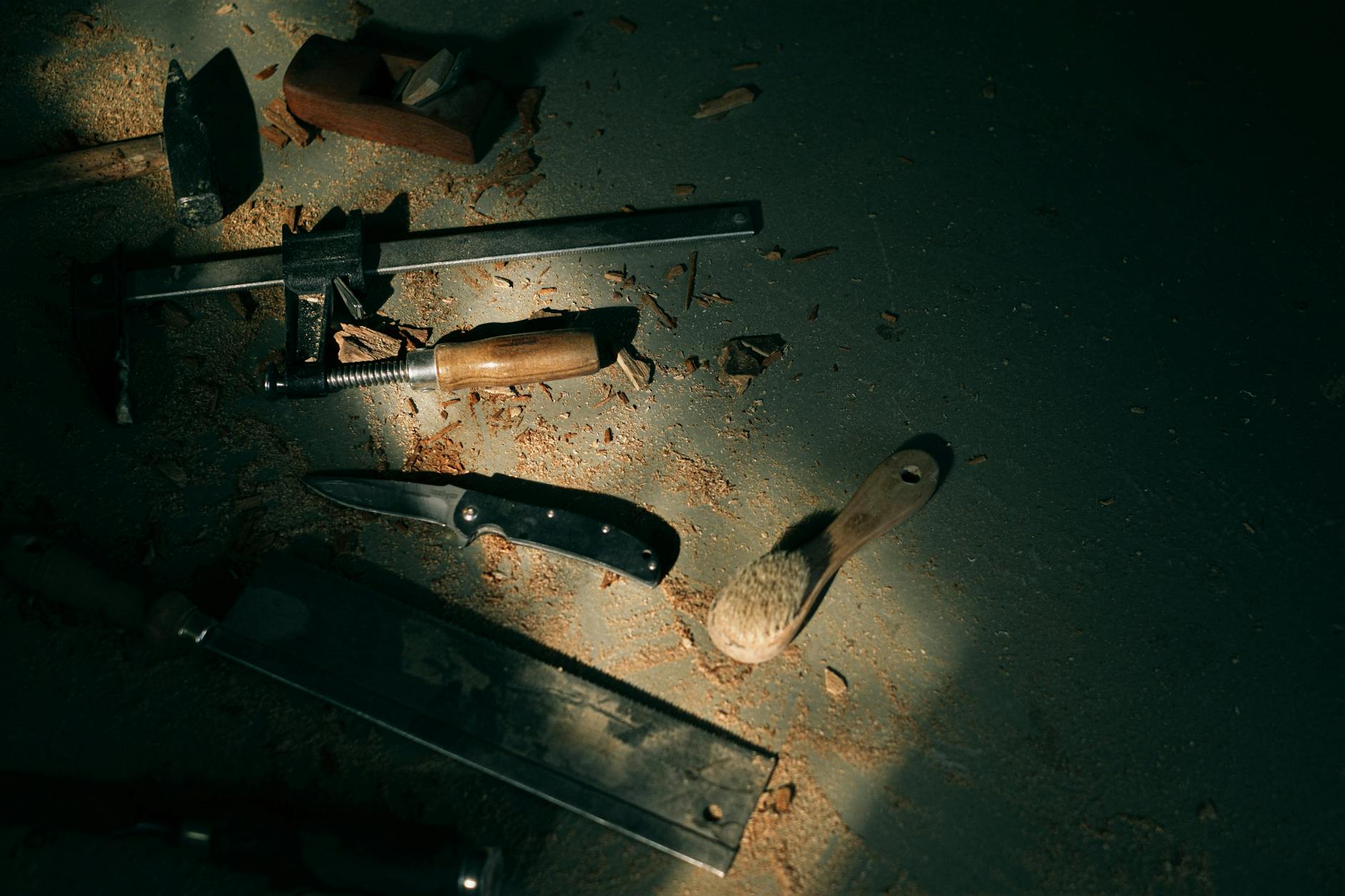 Assorted hand tools scattered on a workshop floor with dramatic lighting, highlighting woodworking crafts.