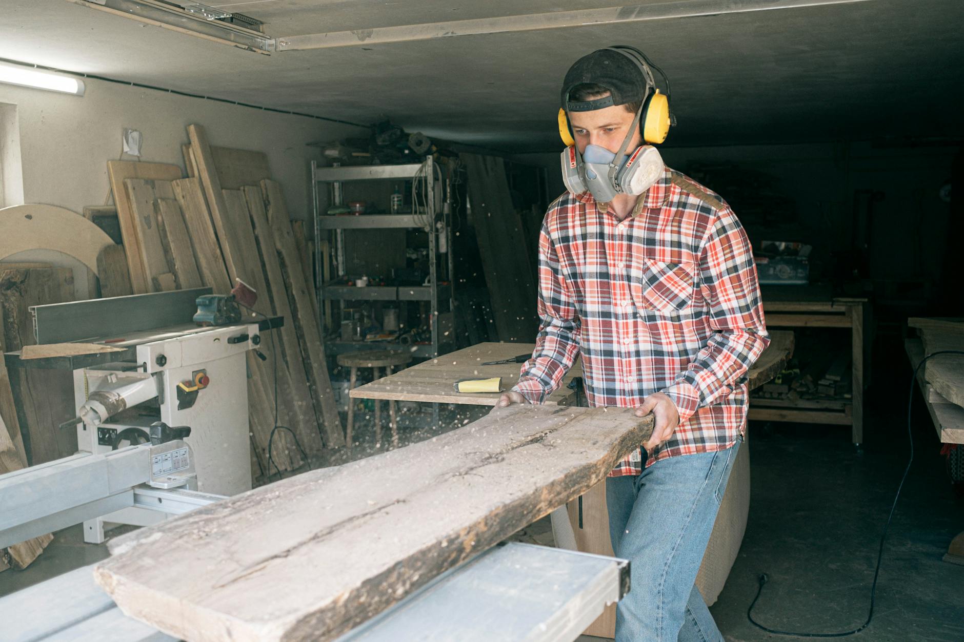 Male woodworker using a saw in a workshop, wearing protective gear to ensure safety during woodworking.