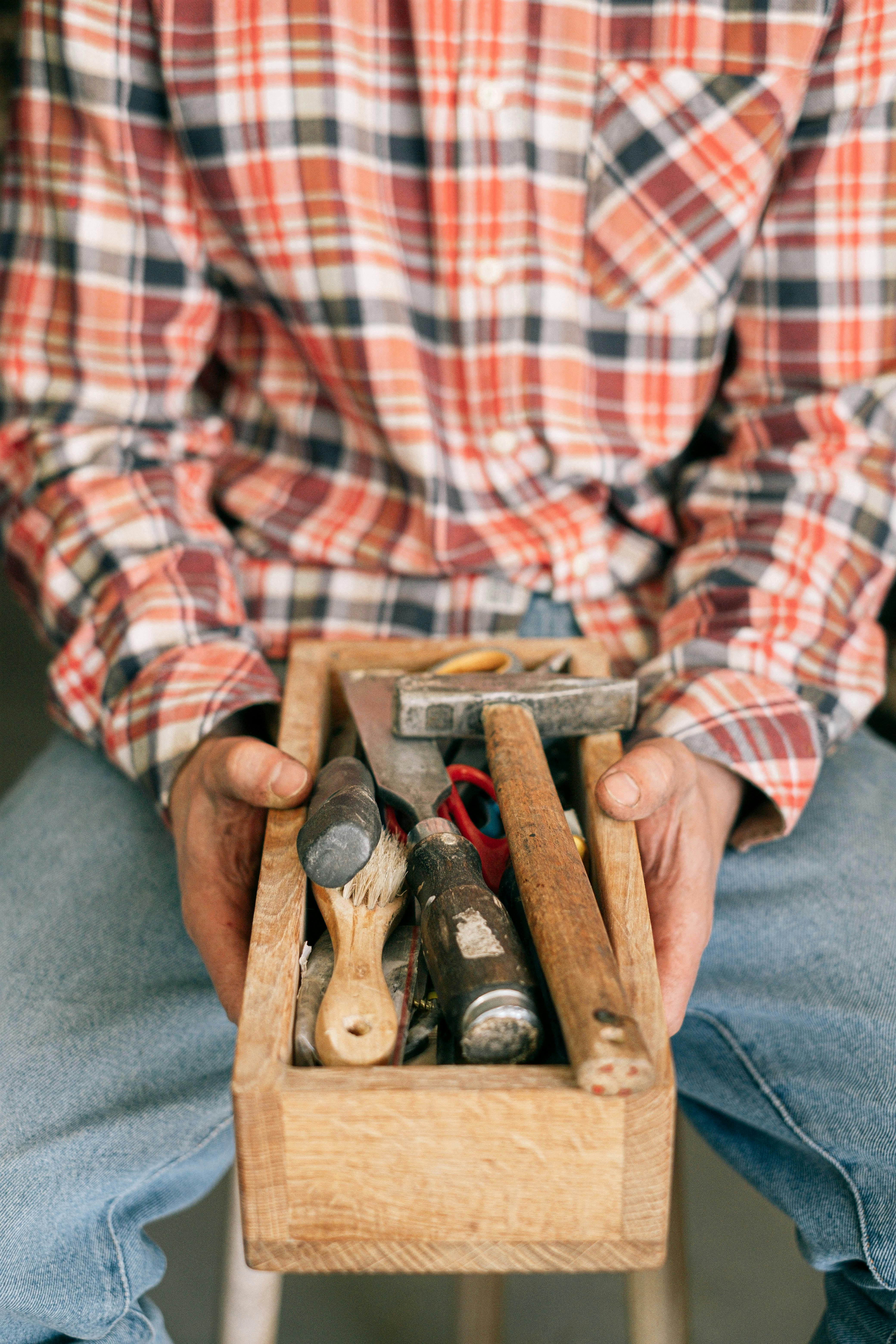 Close-up of a carpenter holding a wooden toolbox filled with various tools.