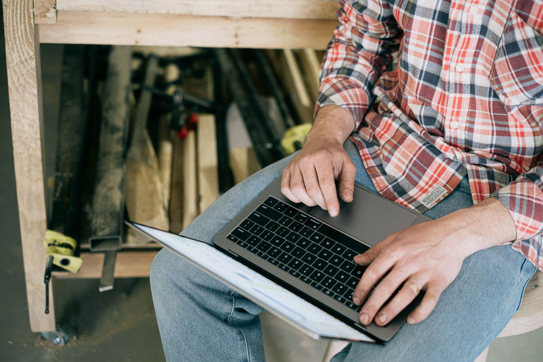 Craftsman working on laptop in woodworking workshop, surrounded by tools.