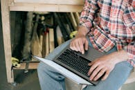 工匠在木工车间里，被工具包围着，在笔记本电脑上工作