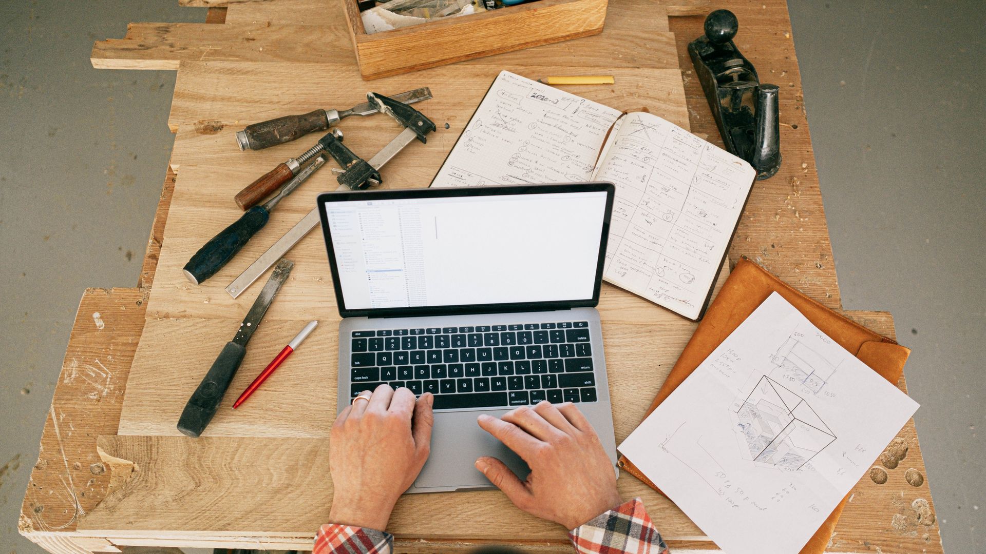 Carpenter using laptop for woodwork designs at a workbench in a workshop — top popular tools