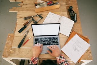 A Person Using a Laptop While on the Carpentry Workbench