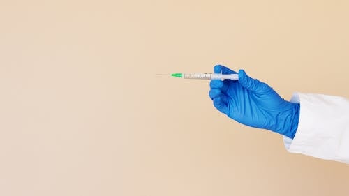 Crop nurse with syringe on beige background