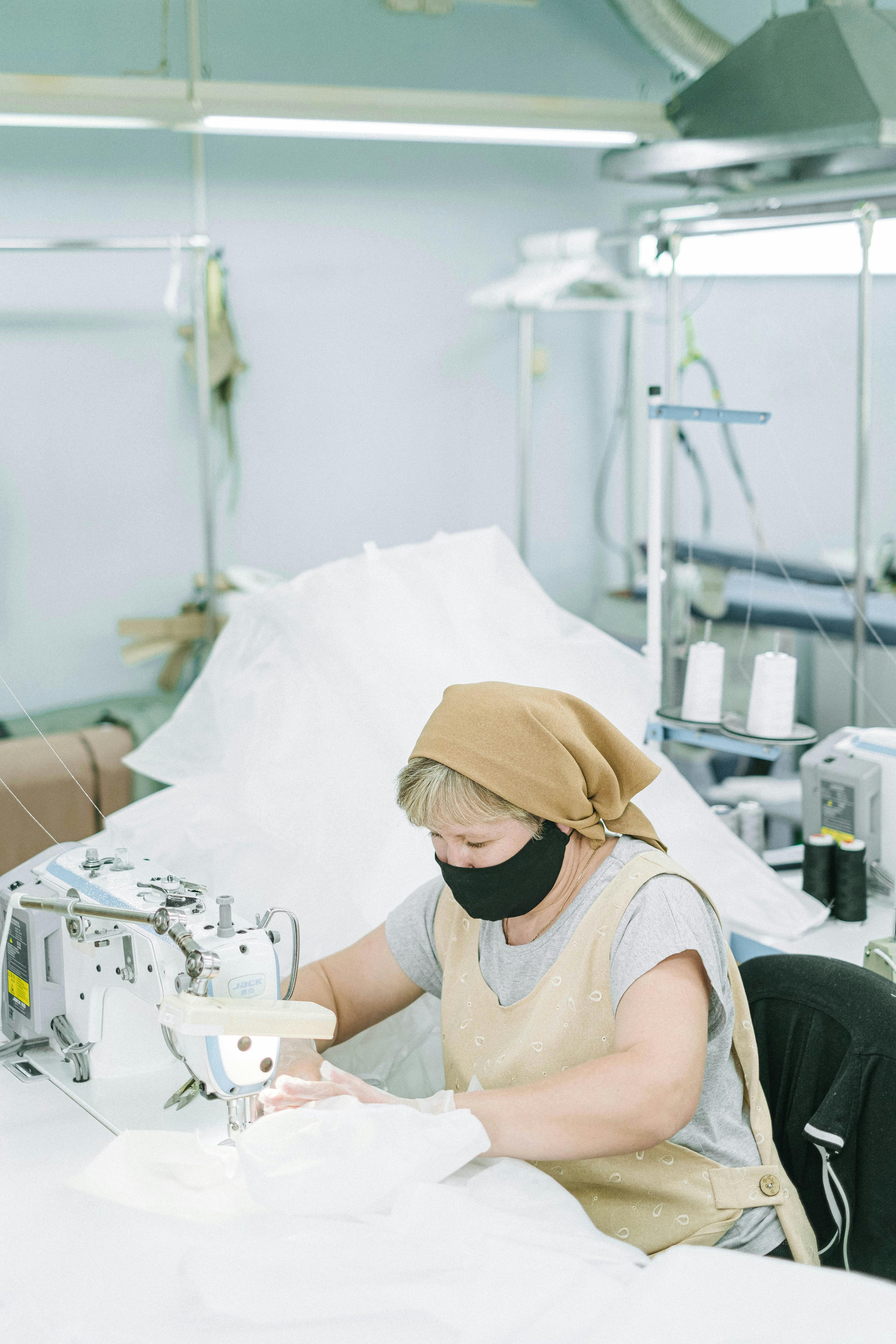 a woman wearing a bandana and a black face mask using a sewing machine