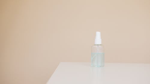 Small plastic bottle of hand antiseptic on white table near light brown wall
