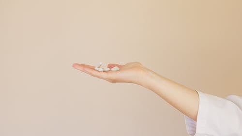 Crop female pharmacist with pile of white pills on palm