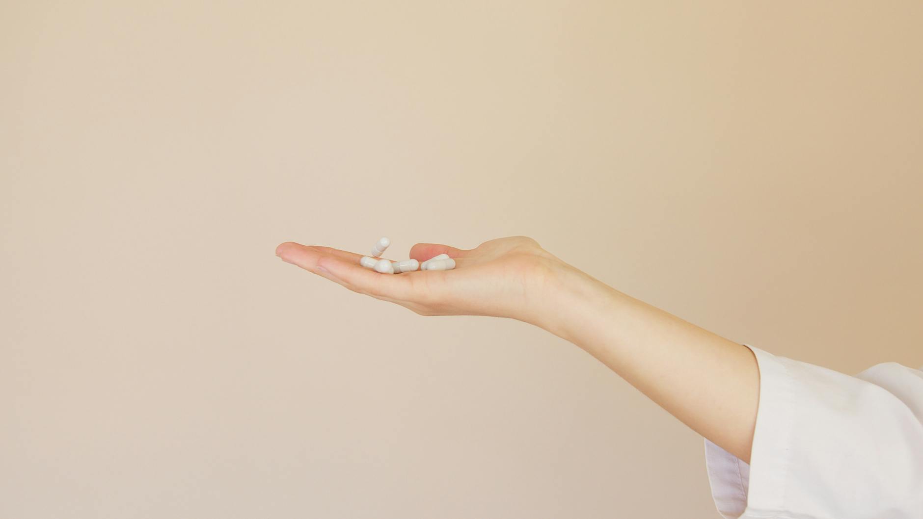 Crop female pharmacist with pile of white pills on palm