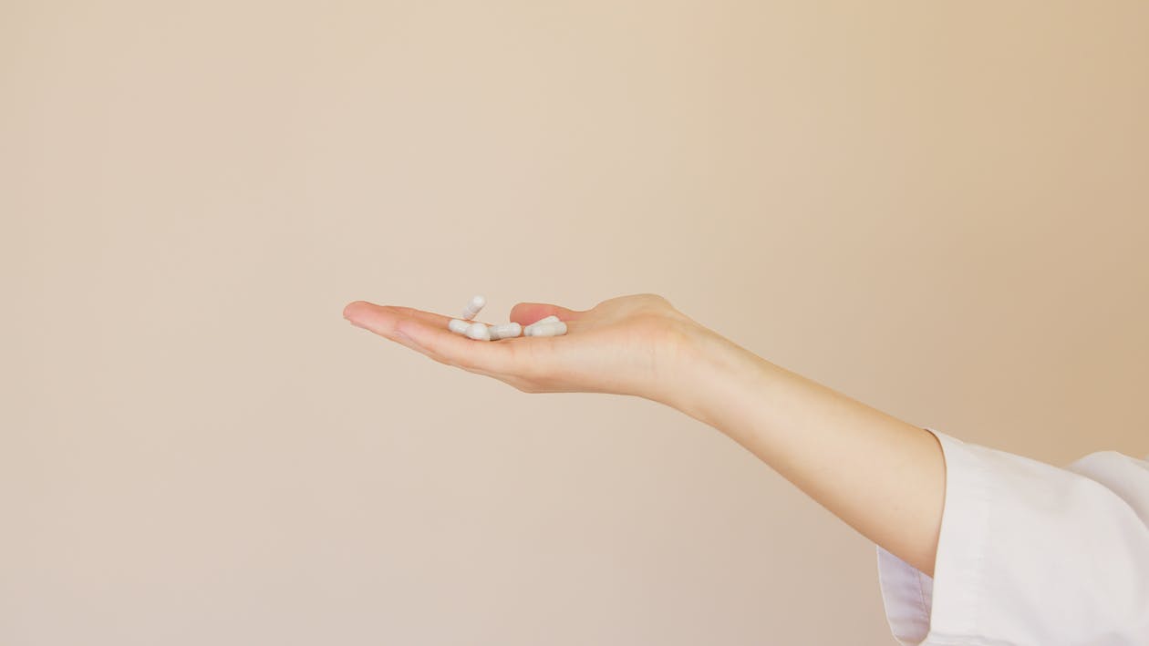 Crop female pharmacist with pile of white pills on palm