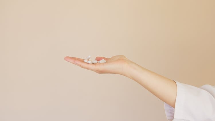 Crop Female Pharmacist With Pile Of White Pills On Palm