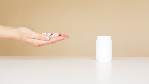 Free Side view of crop unrecognizable person with palm full of double colored pills near table with white plastic jar Stock Photo