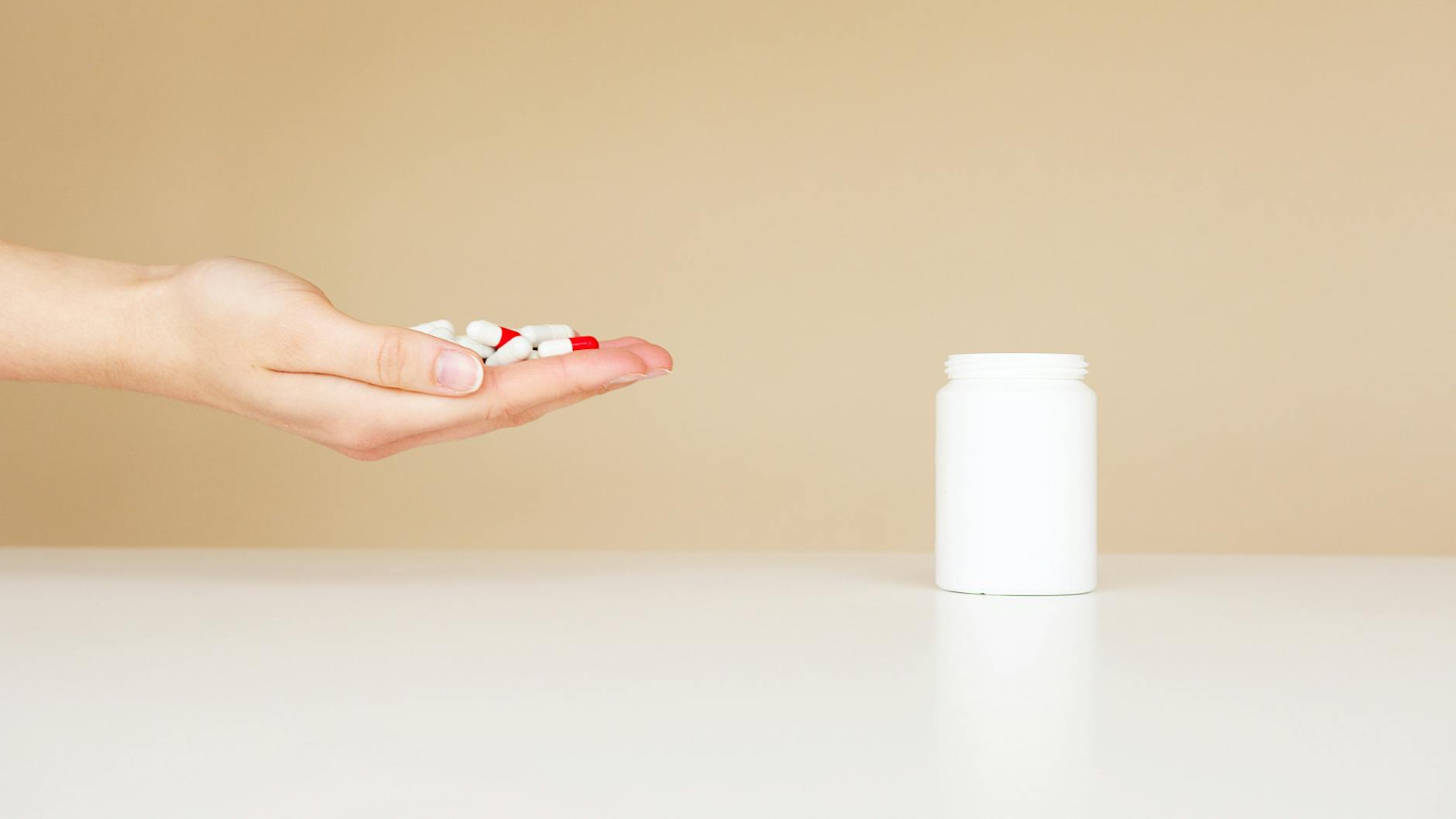 Side view of crop unrecognizable person with palm full of double colored pills near table with white plastic jar