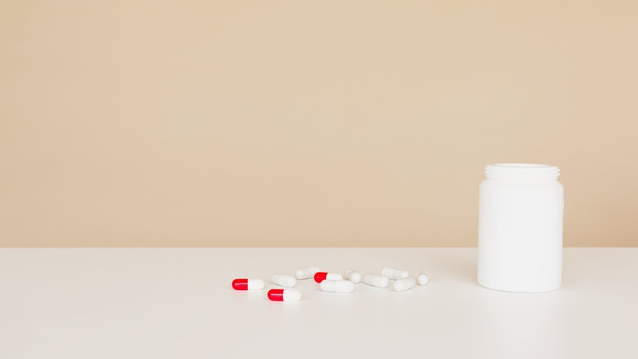 White plastic bottle and pile of double colored pills on white table against light brown background