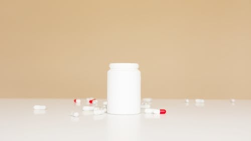 Free Open white plastic bottle and red and white pills scattered around on white table Stock Photo