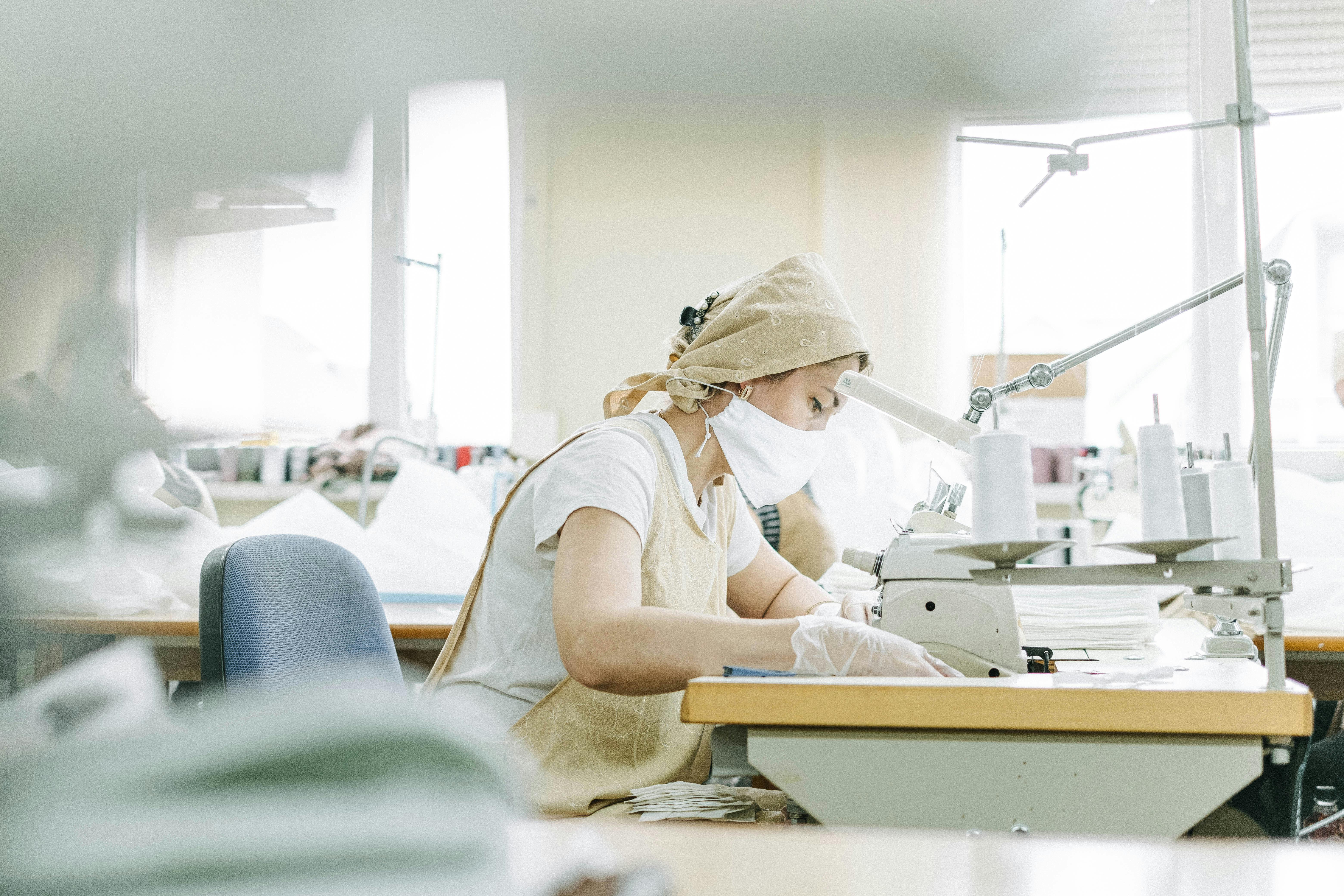 a woman wearing a beige bandana and apron using a sewing machine