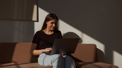 Positive woman surfing internet on laptop on sofa