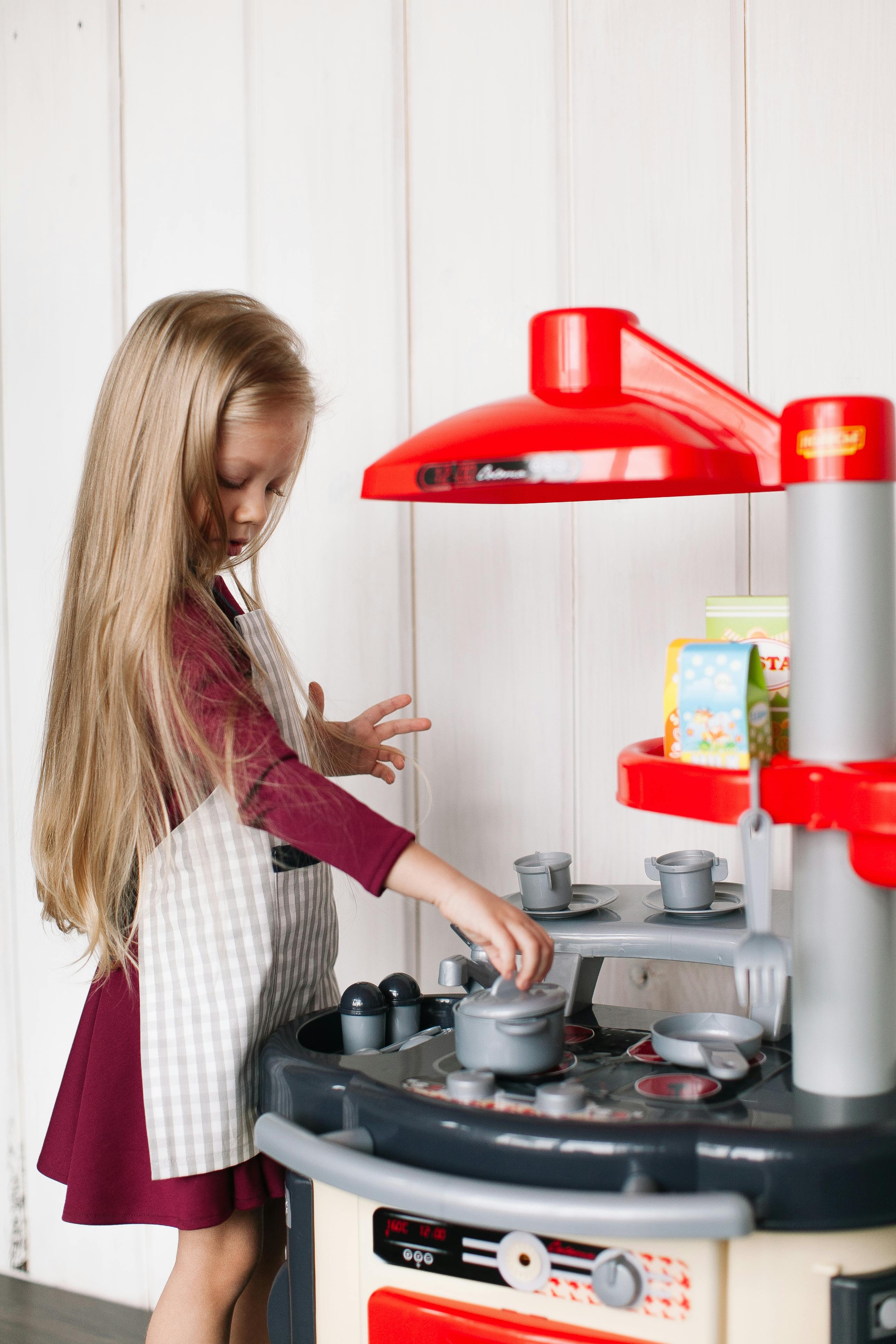 a girl playing with plastic cooking pot on a miniature kitchen