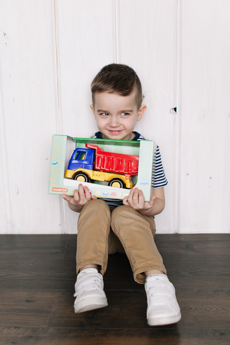 A Boy Holding A Toy Truck In A Box