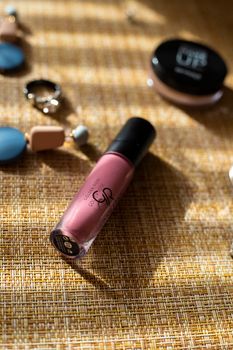 A chic display of lipstick and accessories on textured surface with dramatic shadows.