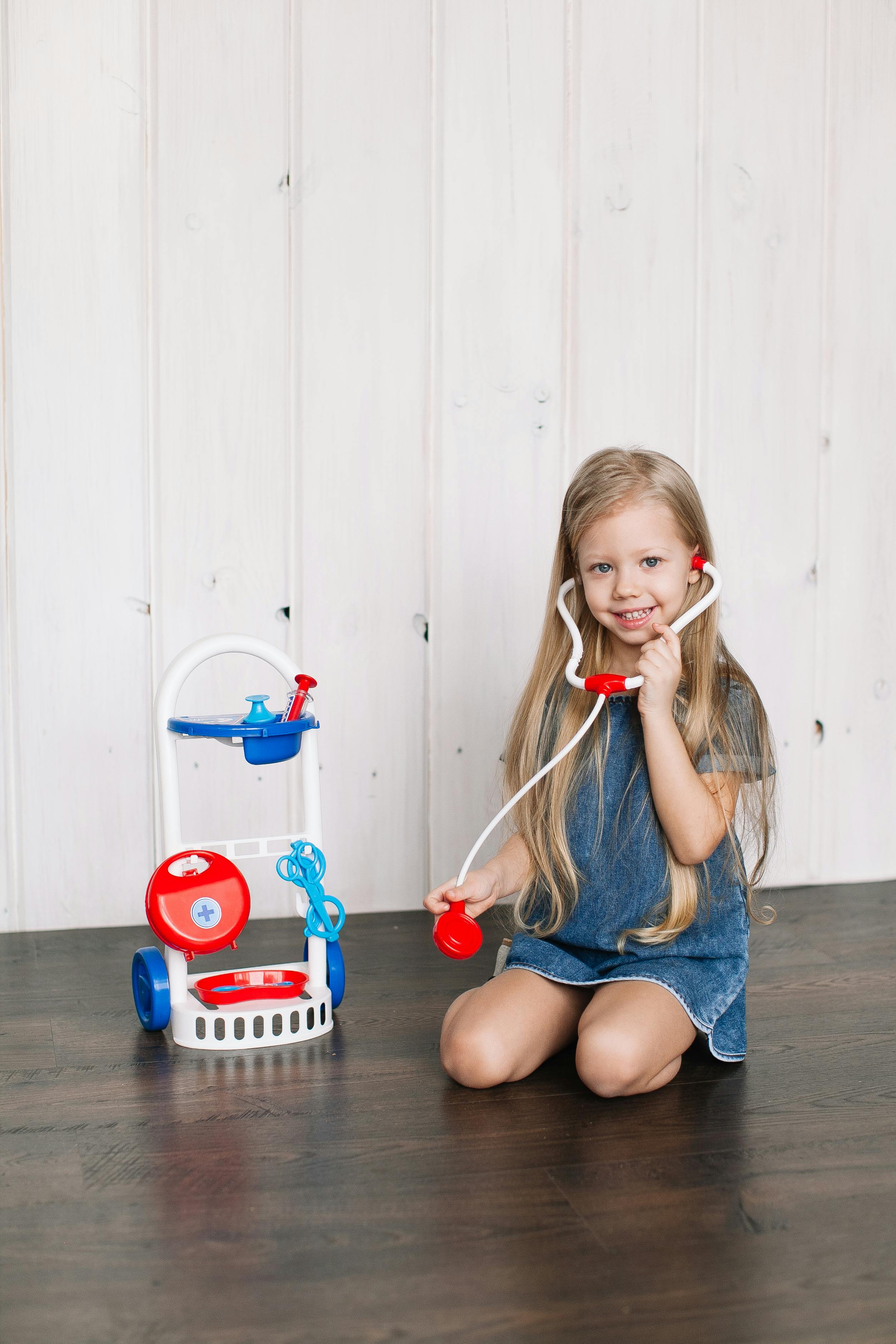 girl in blue denim shorts sitting on floor with a stethoscope plastic toy