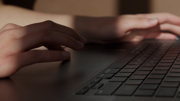 Close-up of hands typing on a laptop, indicating work or study in an office environment.