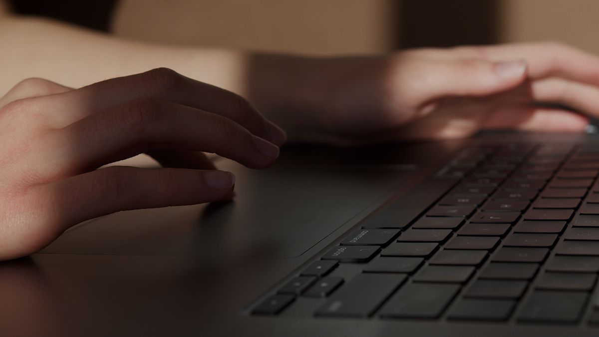 Faceless person working on laptop, representing realistic effort behind no-face online income