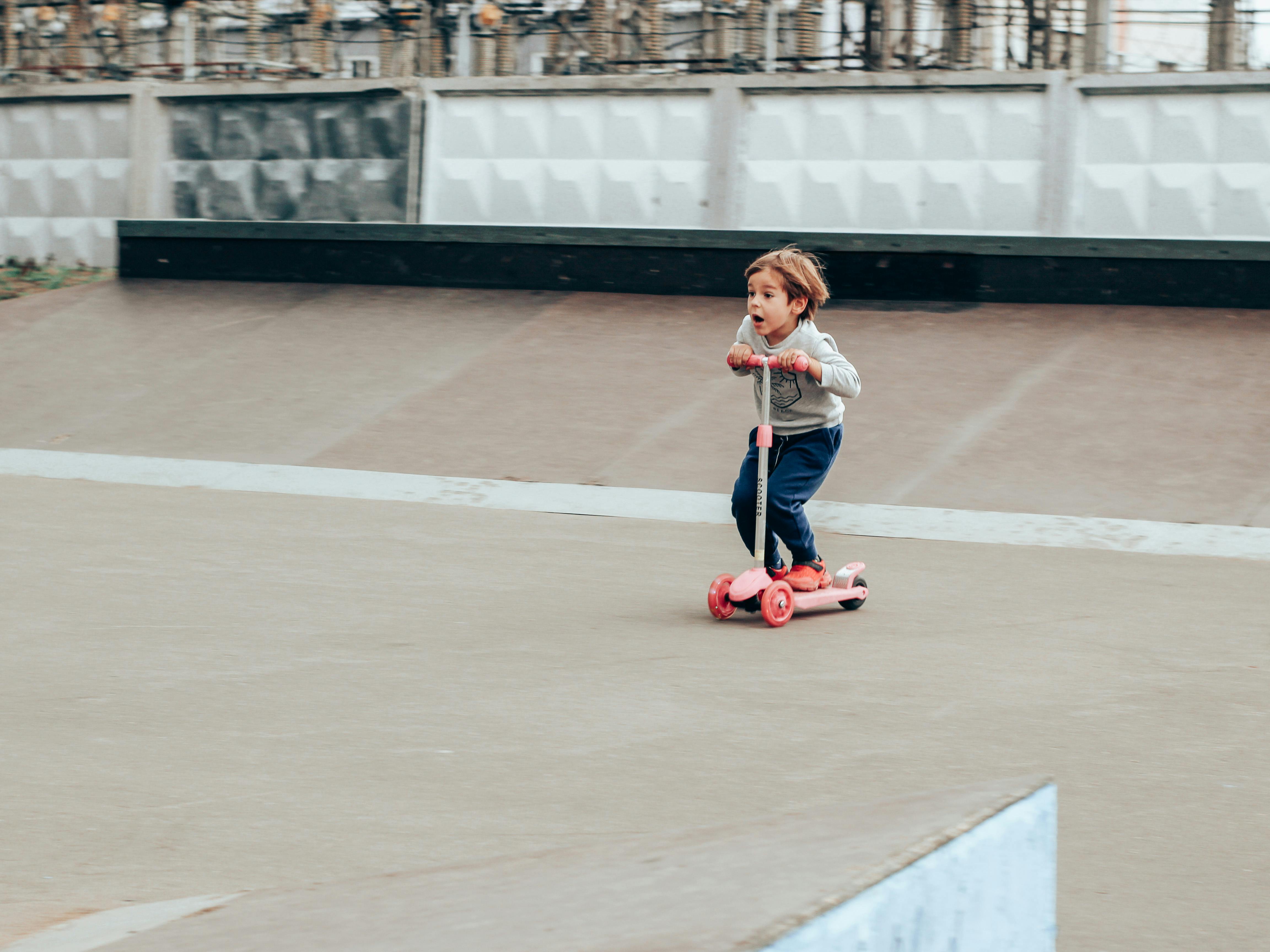 Amazed little boy riding kickboard scooter in skate park
