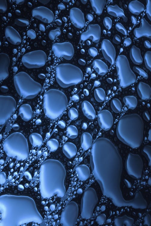 Top view closeup of water drops of various shapes spread on blue surface as abstract background